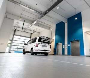 Auch bei Schietwetter. Ein privater Minibus mit Fahrradträger in einer Halle, es ist ein Garagentor und zwei angrenzende Fahrstühle zu sehen.